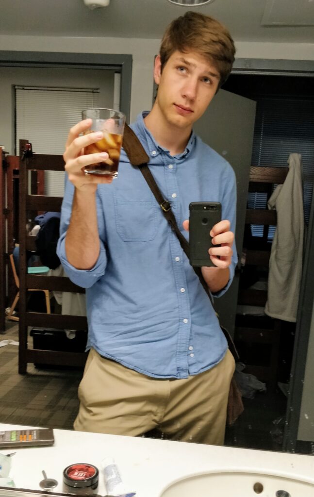 Matthew Krupczak looking in a mirror holding iced coffee